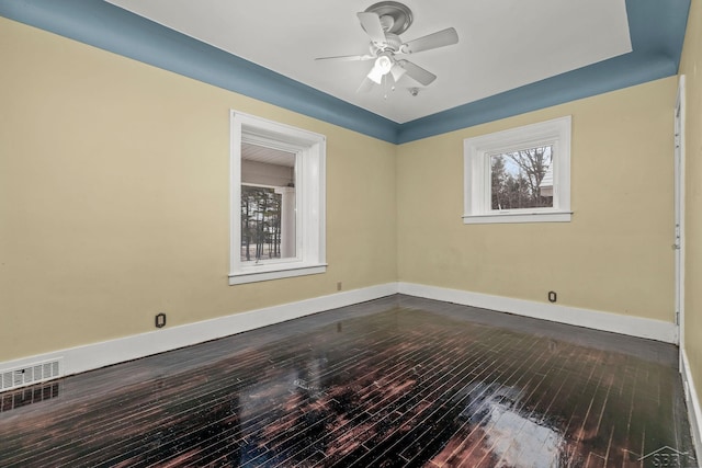 empty room featuring dark wood-style flooring, visible vents, ceiling fan, and a healthy amount of sunlight