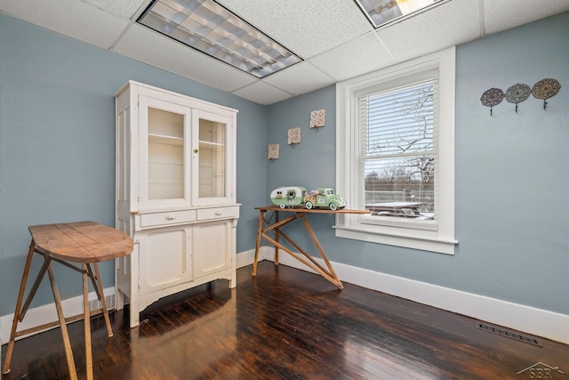 interior space with dark wood-type flooring, a paneled ceiling, visible vents, and baseboards