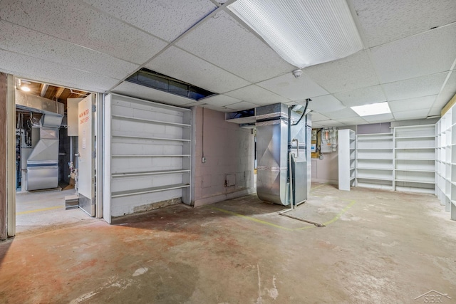 unfinished basement featuring a paneled ceiling and heating unit