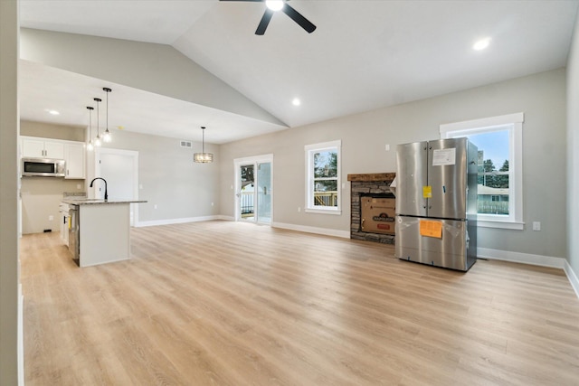 unfurnished living room featuring light wood-type flooring, ceiling fan, a fireplace, and baseboards