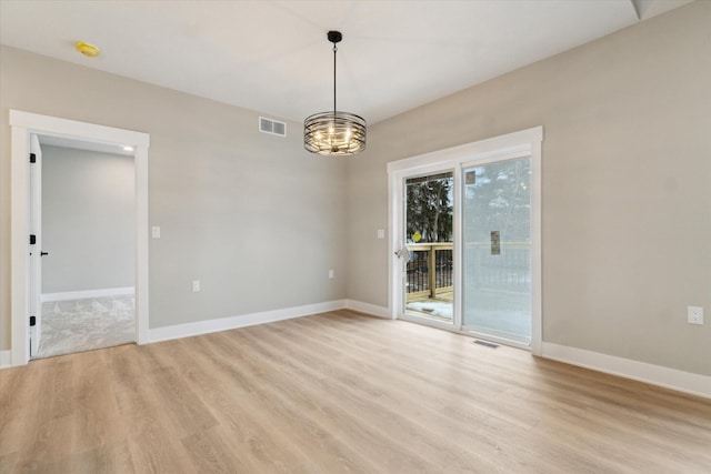 spare room with baseboards, light wood finished floors, visible vents, and an inviting chandelier