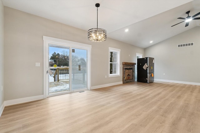 unfurnished living room with visible vents, baseboards, light wood-style flooring, vaulted ceiling, and a stone fireplace