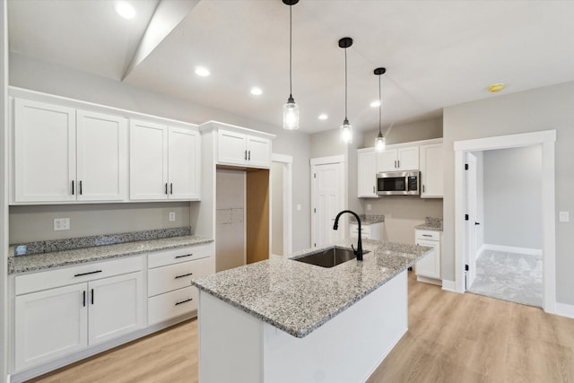 kitchen with light wood finished floors, stainless steel microwave, a sink, and white cabinetry