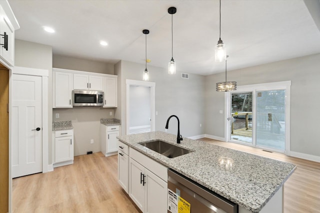 kitchen with light wood-style flooring, appliances with stainless steel finishes, white cabinetry, a sink, and light stone countertops