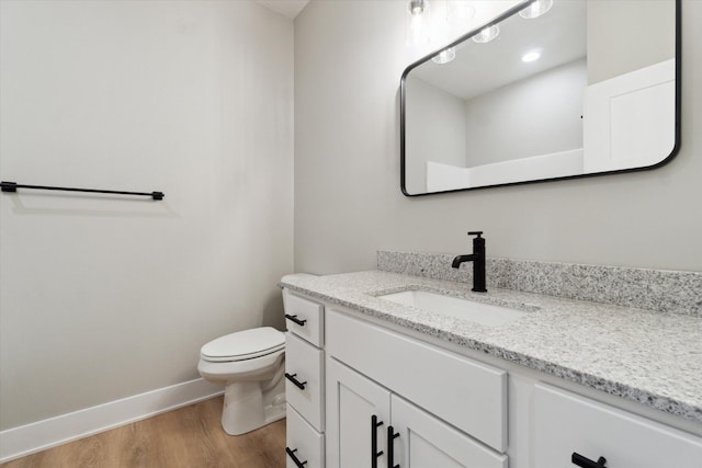 bathroom featuring toilet, baseboards, wood finished floors, and vanity