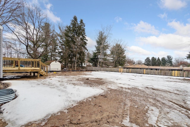 yard layered in snow with an outbuilding, a fenced backyard, and a wooden deck