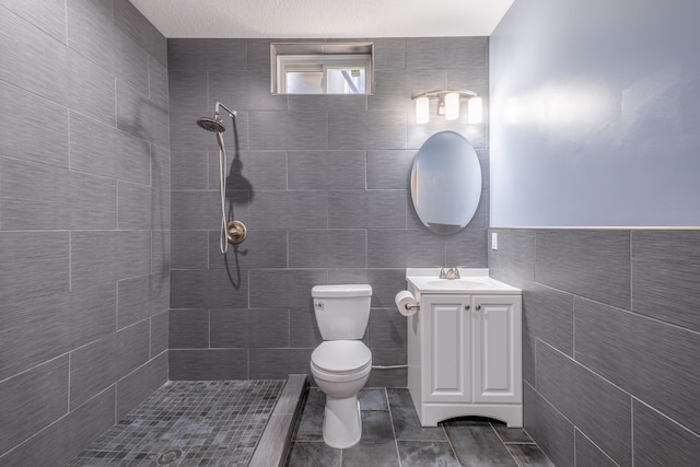 bathroom featuring a tile shower, toilet, tile walls, and vanity