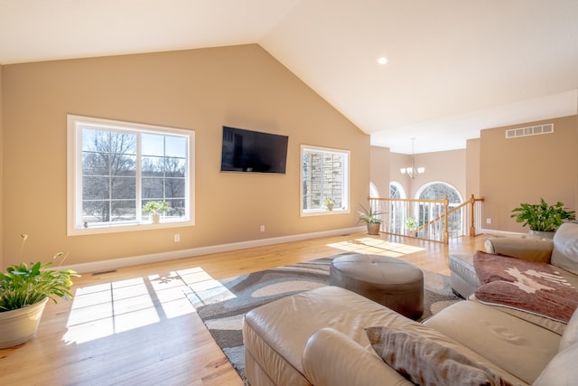 living area with a notable chandelier, light wood-style flooring, high vaulted ceiling, and visible vents