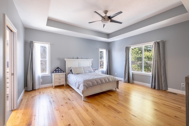 bedroom with visible vents, baseboards, ceiling fan, light wood-type flooring, and a tray ceiling