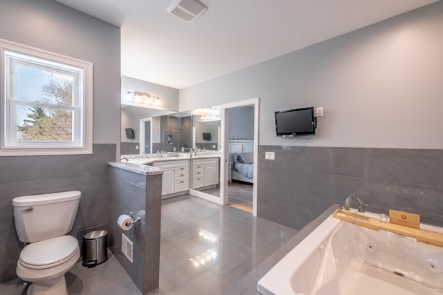 full bath with visible vents, toilet, a jetted tub, tile walls, and vanity