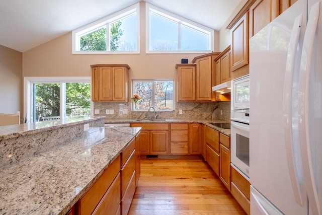 kitchen featuring under cabinet range hood, a sink, white appliances, light wood-style floors, and decorative backsplash