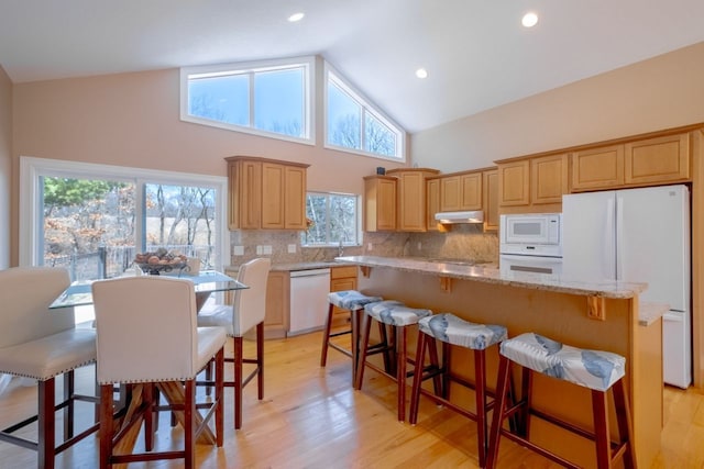 kitchen featuring a center island, under cabinet range hood, light wood-type flooring, decorative backsplash, and white appliances