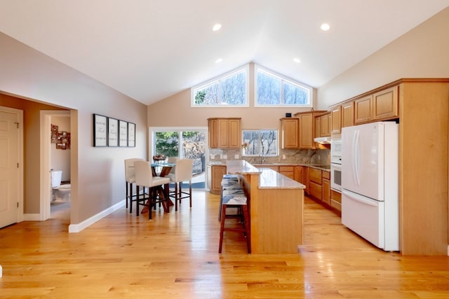 kitchen featuring white appliances, light wood finished floors, a kitchen breakfast bar, backsplash, and a center island