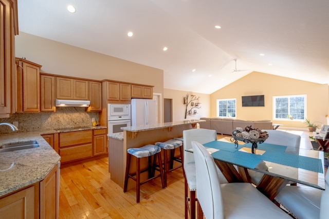 kitchen with white appliances, a breakfast bar, a sink, under cabinet range hood, and open floor plan