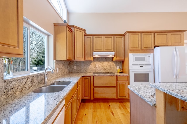 kitchen featuring under cabinet range hood, a sink, white appliances, decorative backsplash, and light stone countertops