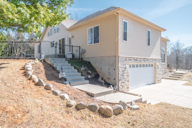 view of side of home with stairway, driveway, roof with shingles, and an attached garage