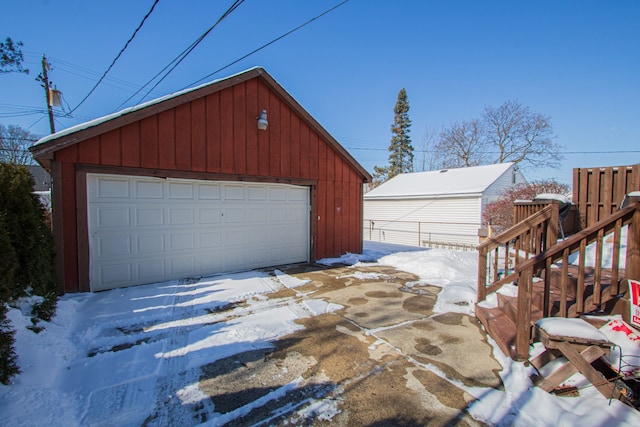 snow covered garage featuring a garage and fence