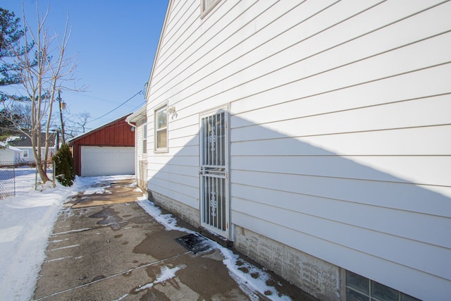 view of snowy exterior with an outdoor structure, fence, and a detached garage