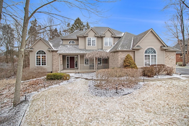 traditional home with brick siding, covered porch, and roof with shingles