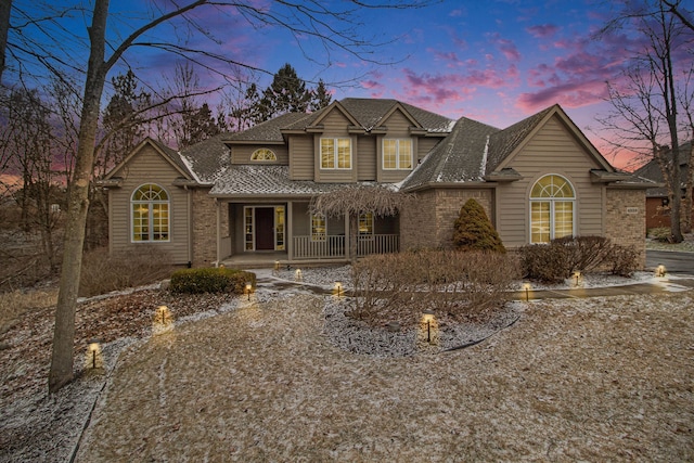 traditional-style house featuring a porch, brick siding, and roof with shingles