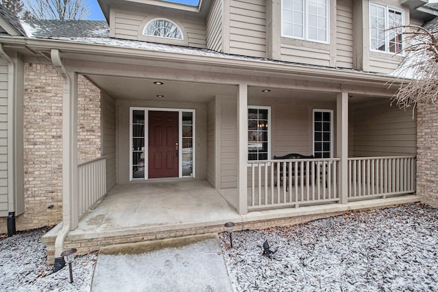 view of exterior entry with brick siding and covered porch