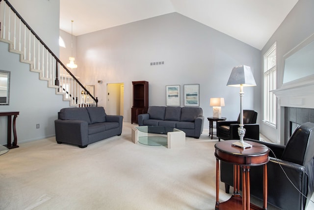 carpeted living room with stairway, baseboards, visible vents, high vaulted ceiling, and a tile fireplace