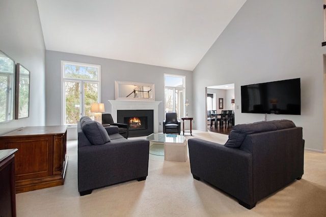 living area with light colored carpet, a warm lit fireplace, and high vaulted ceiling