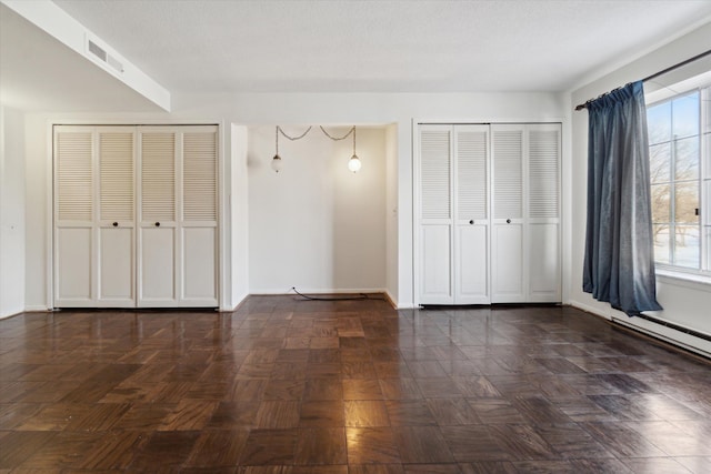 unfurnished bedroom with visible vents, a textured ceiling, baseboards, and two closets