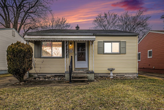 bungalow-style home with a shingled roof and a lawn