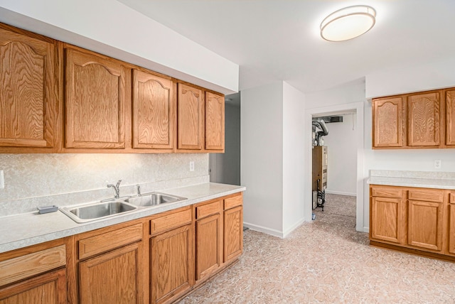 kitchen featuring brown cabinetry, baseboards, light countertops, and a sink