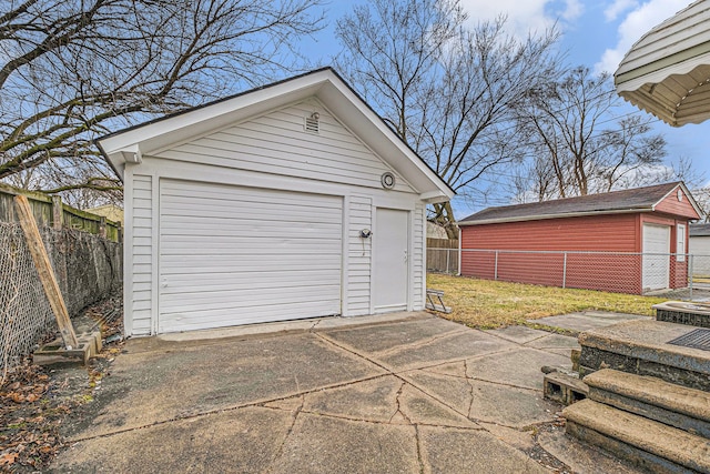 detached garage featuring concrete driveway and fence