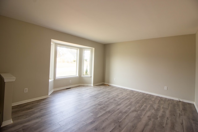 unfurnished living room with dark wood-style flooring, visible vents, and baseboards