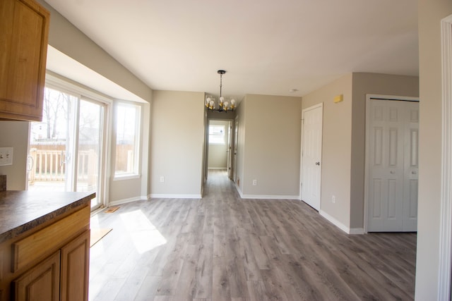 unfurnished dining area with a chandelier, light wood-type flooring, and baseboards