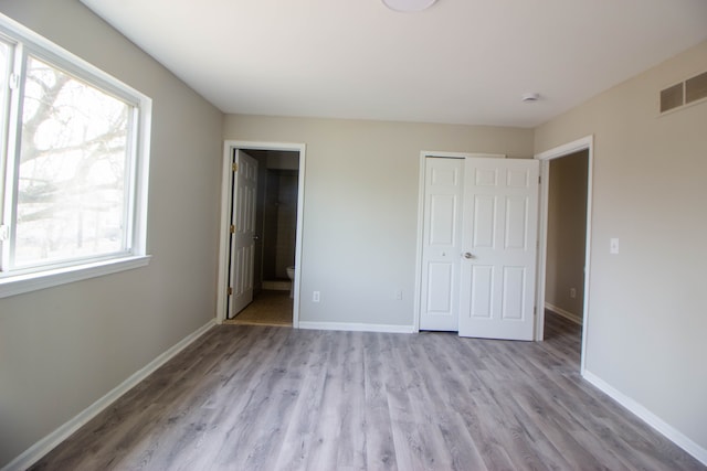 unfurnished bedroom with a closet, visible vents, ensuite bathroom, wood finished floors, and baseboards