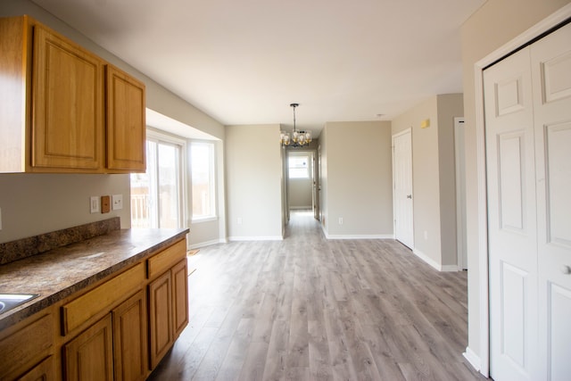 kitchen with dark countertops, brown cabinetry, light wood-type flooring, and a notable chandelier