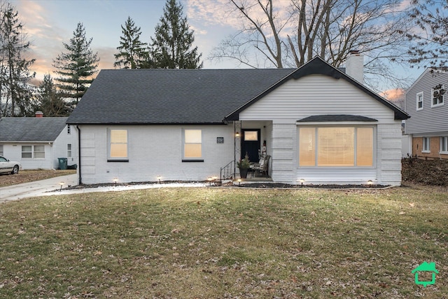 view of front facade featuring roof with shingles, a front lawn, and brick siding