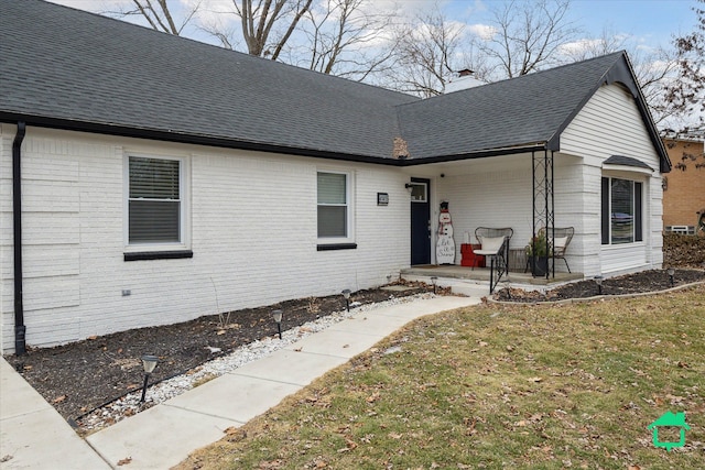 view of front of house featuring a front yard, brick siding, a chimney, and roof with shingles