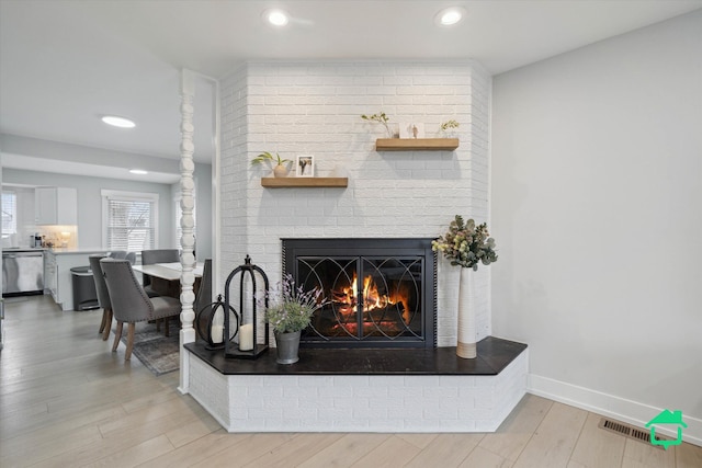 living area featuring light wood-type flooring, a brick fireplace, visible vents, and baseboards