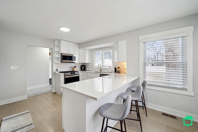 kitchen with stainless steel appliances, a peninsula, visible vents, tasteful backsplash, and a kitchen bar