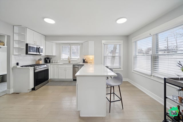 kitchen featuring a peninsula, a sink, appliances with stainless steel finishes, decorative backsplash, and a kitchen bar