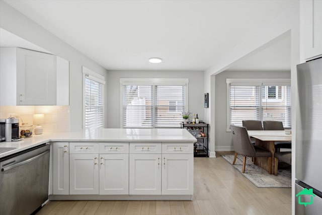 kitchen featuring stainless steel appliances, a peninsula, white cabinetry, light countertops, and tasteful backsplash