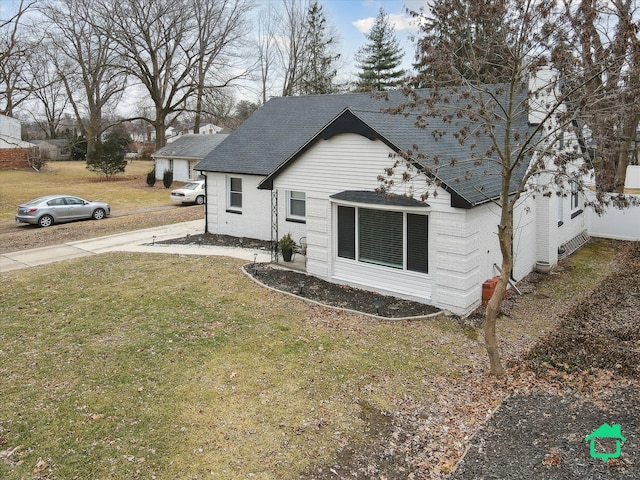 exterior space featuring brick siding, a front yard, and a shingled roof