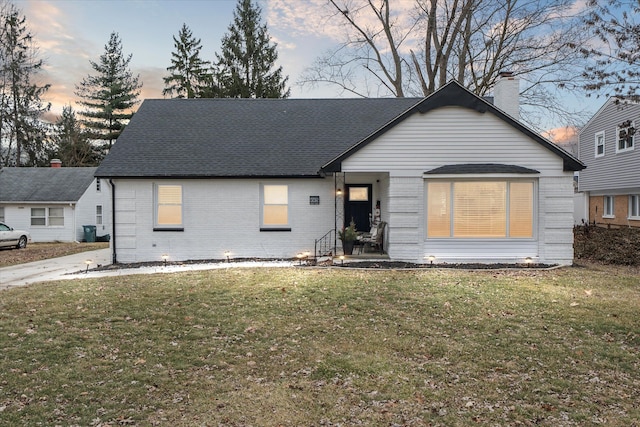 view of front of house with a front yard, brick siding, and a shingled roof