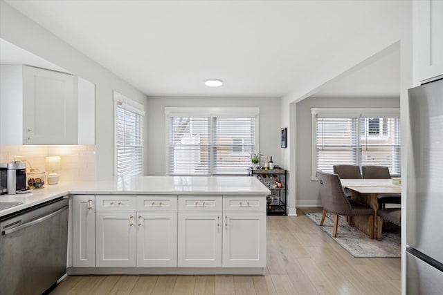 kitchen with tasteful backsplash, white cabinetry, stainless steel appliances, a peninsula, and light countertops