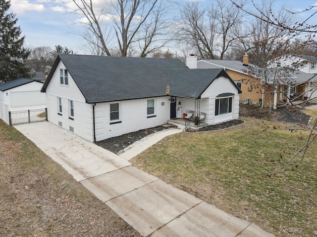 ranch-style house featuring a shingled roof, a front lawn, a chimney, an outbuilding, and driveway