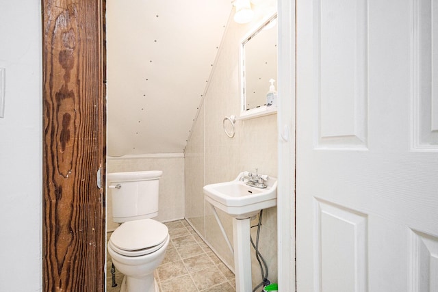 half bathroom featuring toilet, a sink, tile walls, vaulted ceiling, and tile patterned floors