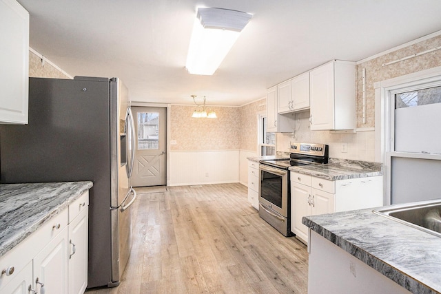 kitchen featuring wainscoting, stainless steel appliances, light wood-style floors, white cabinetry, and a sink