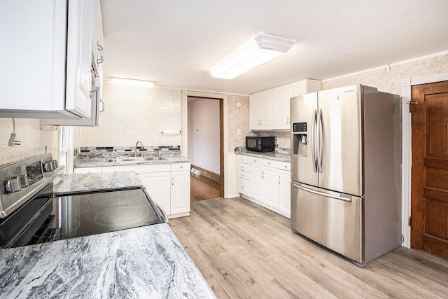 kitchen with a sink, electric stove, stainless steel fridge, and white cabinetry