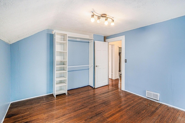 unfurnished bedroom with visible vents, hardwood / wood-style floors, vaulted ceiling, a textured ceiling, and a closet