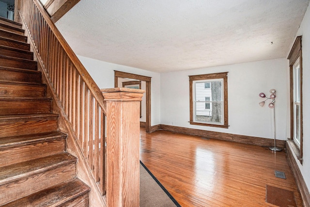 staircase with visible vents, a textured ceiling, baseboards, and wood finished floors